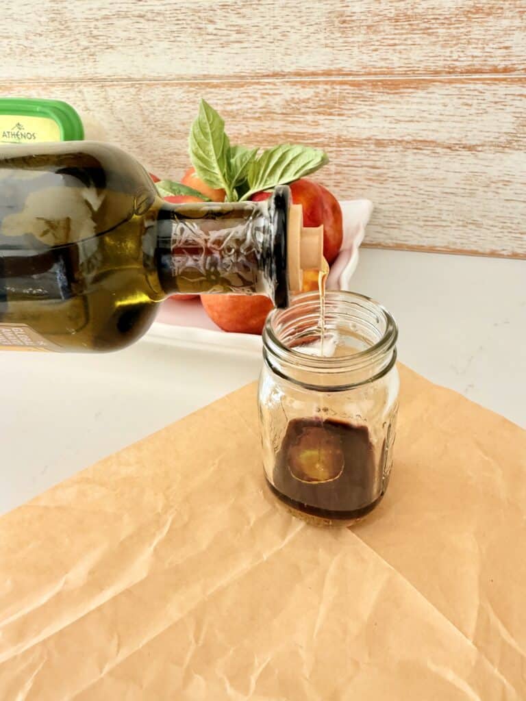 Pouring olive oil into a glass jar on parchment paper on the counter.