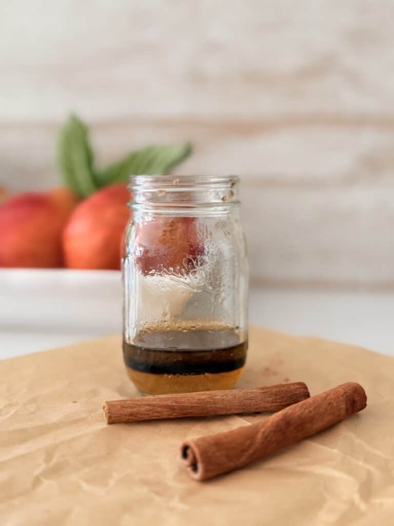 Honey, balsamic vinegar, and olive oil with salt, pepper, and cinnamon a in a glass jar on parchment paper on the counter.