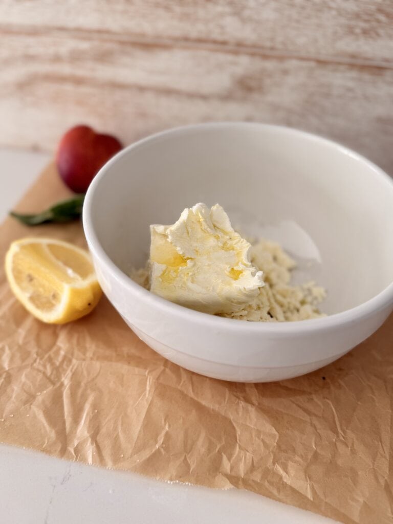 Cream cheese, crumbled, feta olive oil and lemon juice in a white bowl on parchment paper on the counter.