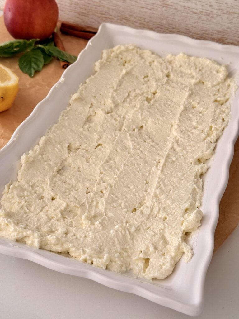 Whipped feta spread out on a flat white platter on the counter.