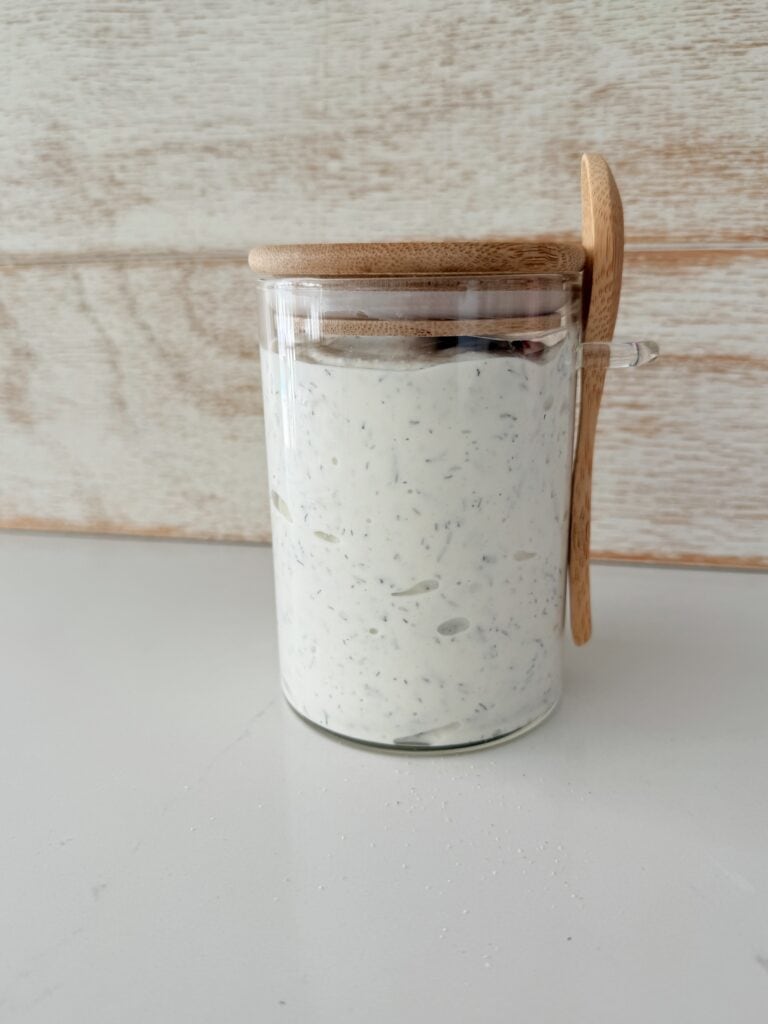 Homemade ranch dressing in a airtight sealed container on the white countertop.