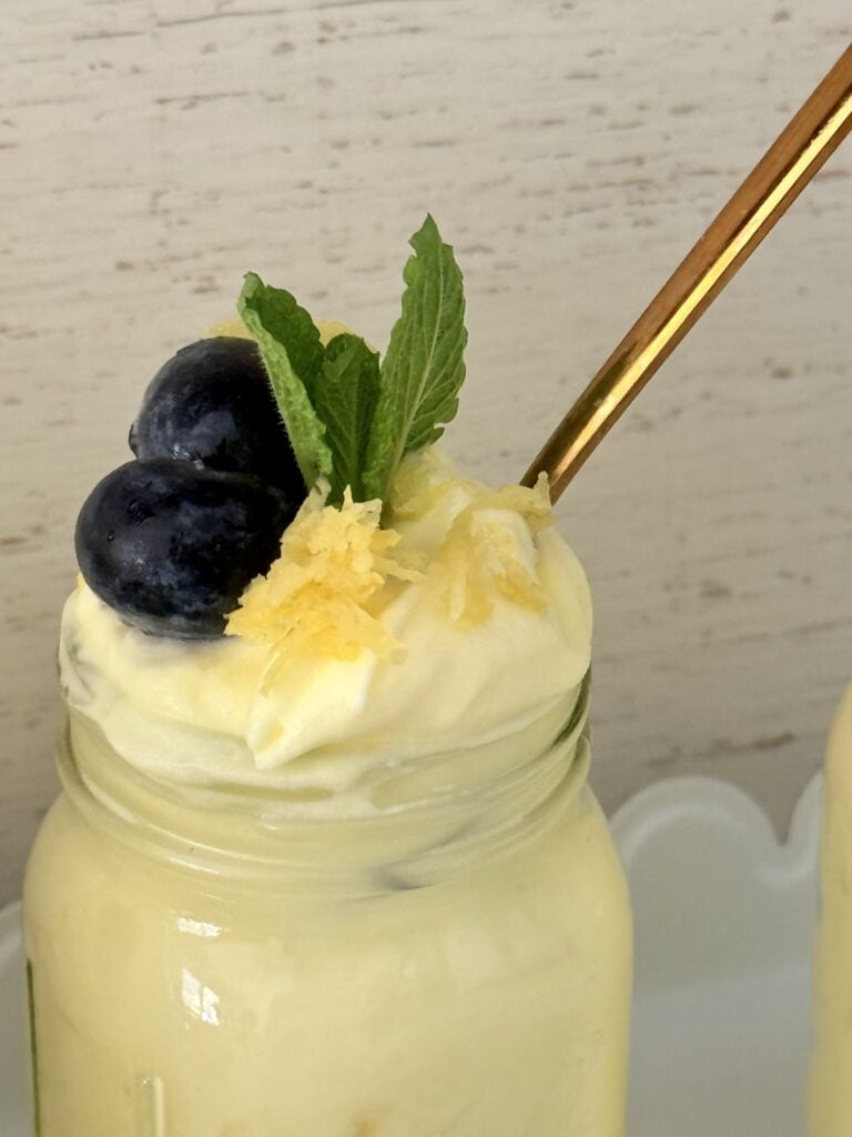 Simple lemon pudding dessert in a glass jar on the counter with a spoon inside of the jar. 