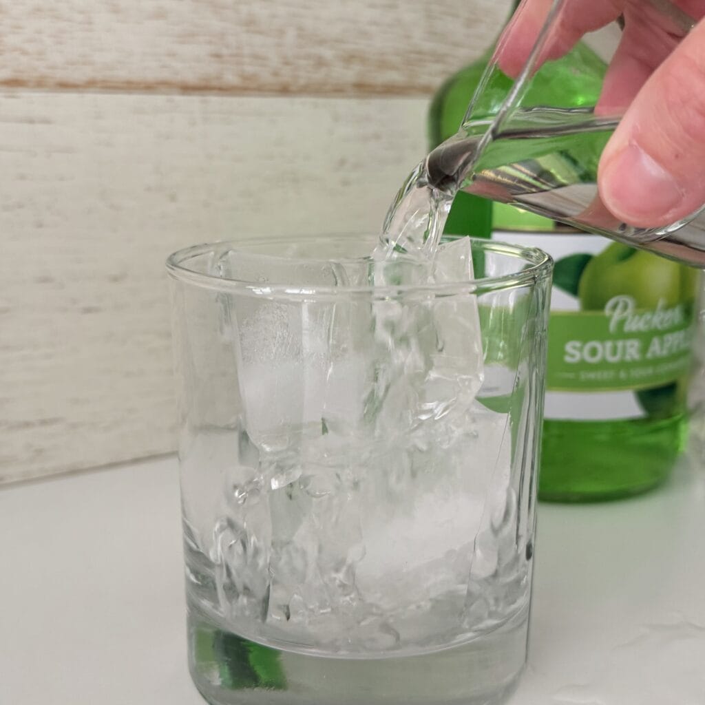 Pouring tequila into a glass with ice on the counter.