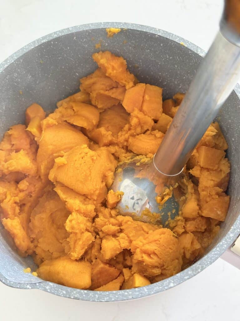 Using a hand mixer to mash sweet potatoes in a pot on the counter.