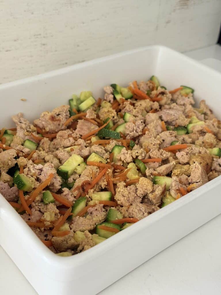 Ground turkey meat that is cooked and softened veggies, zucchini, and carrots in a white baking dish on the counter.