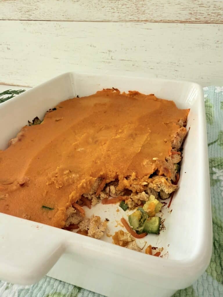 Turkey, sweet potato shepherds pie, and a white baking dish on a floral tea towel on the counter.