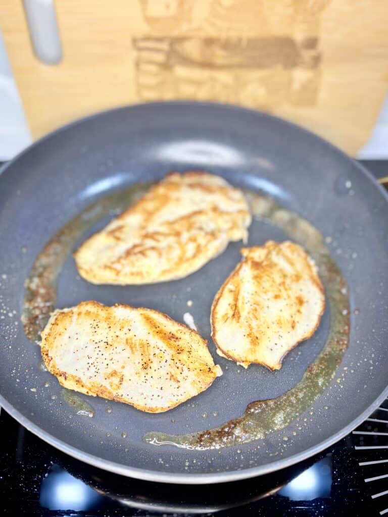 boneless skinless chicken breasts browning in a skillet with olive oil and butter