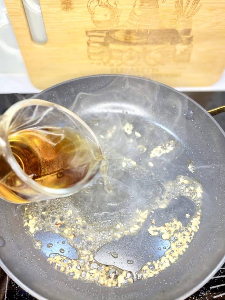 brandy being poured into a hot pan with minced garlic