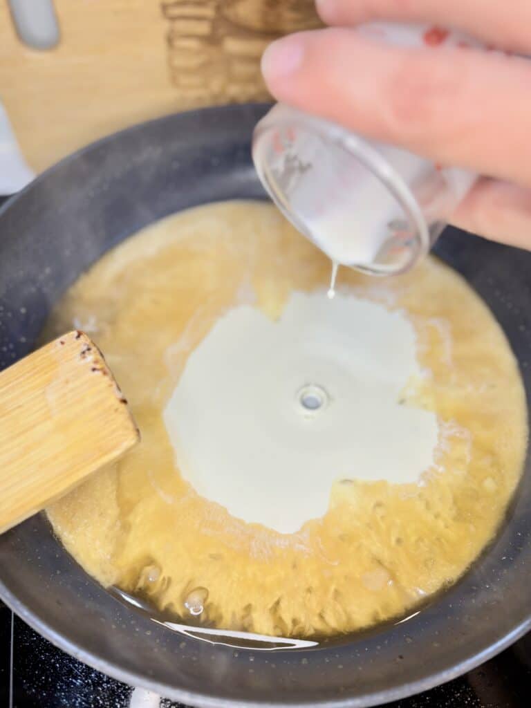 cream being poured into a skillet with brandy and garlic