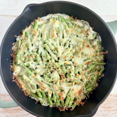 cooked cheesy green beans in a cast iron skillet