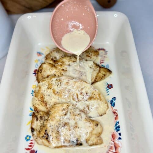 cooked chicken with brandy cream sauce being spooned over top in a casserole dish