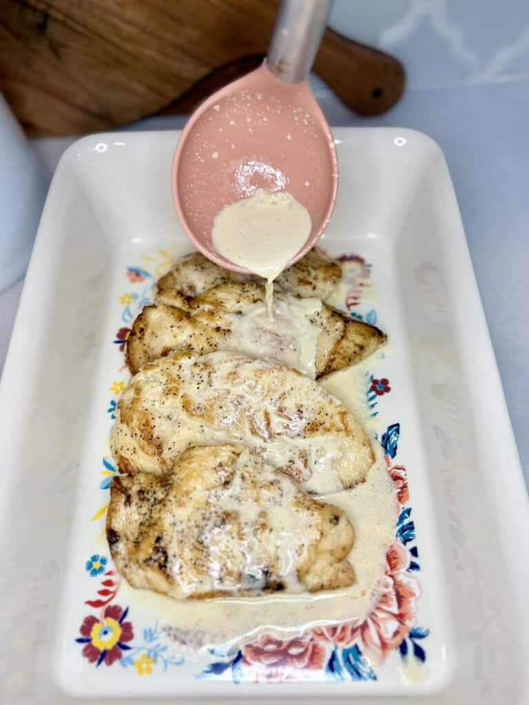 cooked chicken with brandy cream sauce being spooned over top in a casserole dish