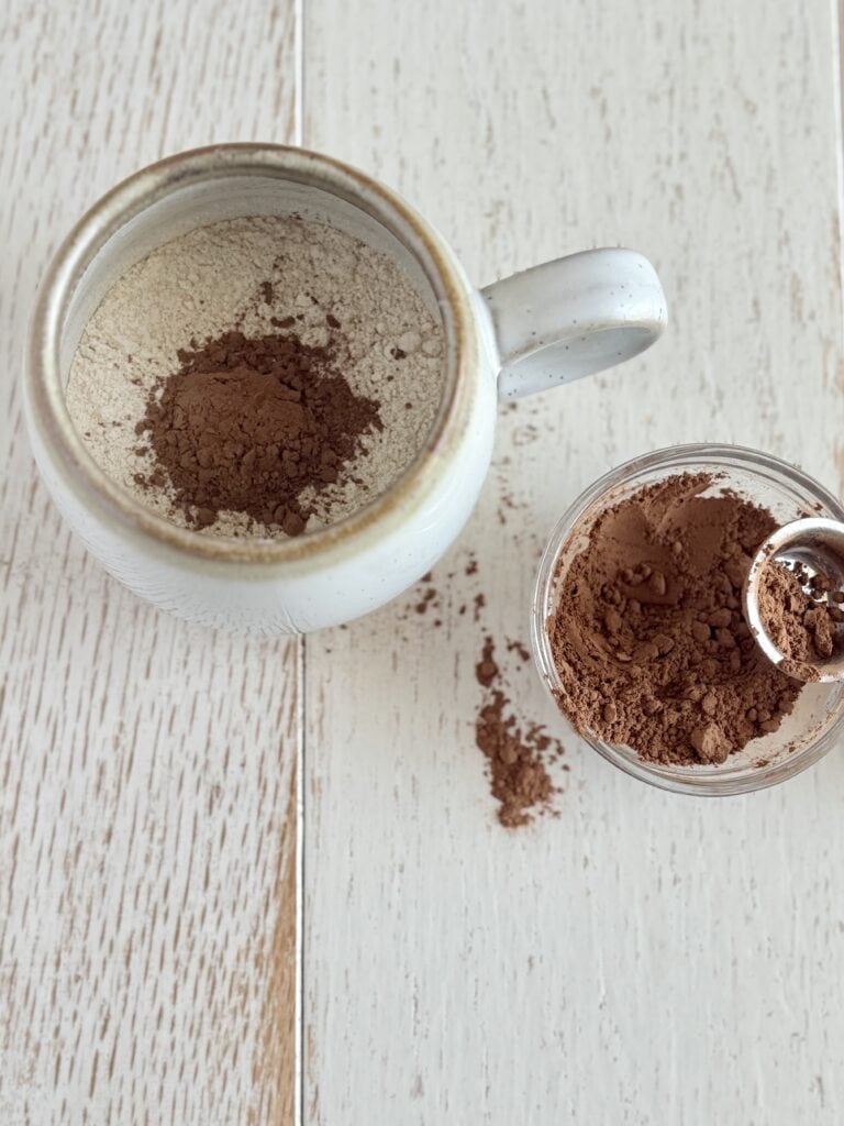 protein pancake mix in a mug with cocoa powder and a small bowl of coconut powder next to it