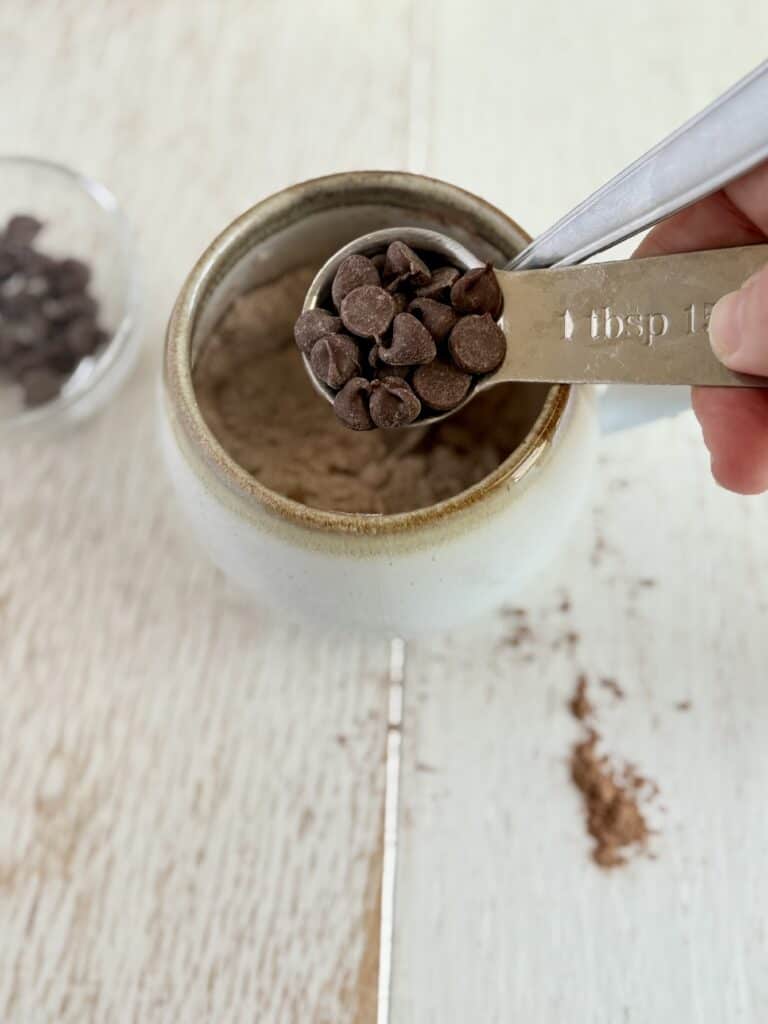 chocolate chips being added to a mug with protein pancake mix and cocoa powder