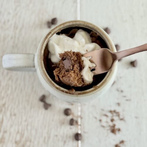 a bite of chocolate muffin on a fork with whipped cream over a mug