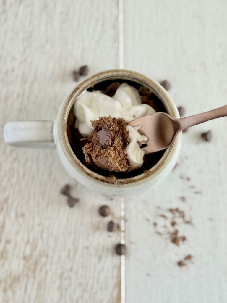 a bite of chocolate muffin on a fork with whipped cream over a mug