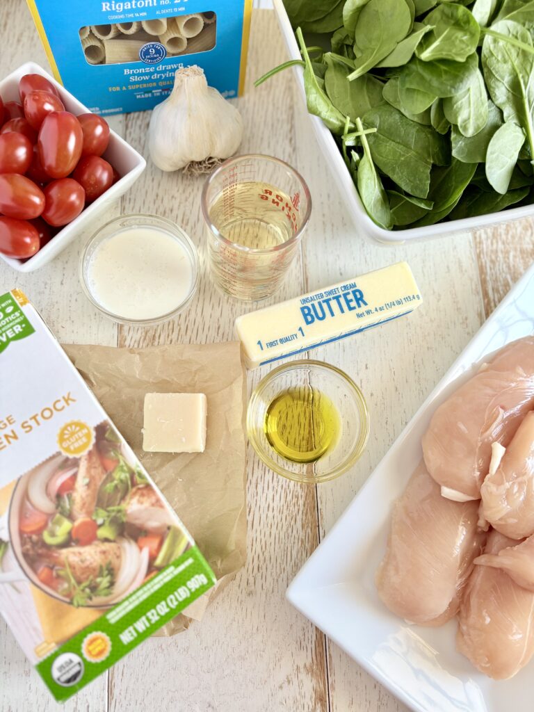 raw chicken, spinach, and tomatoes next to bowls of cream, oil, and wine with chicken broth, butter, parmesan cheese and garlic on a wooden board