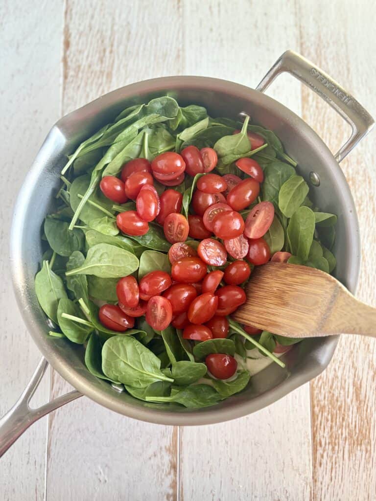 tomatoes and spinach added to a skillet with a wooden spatula