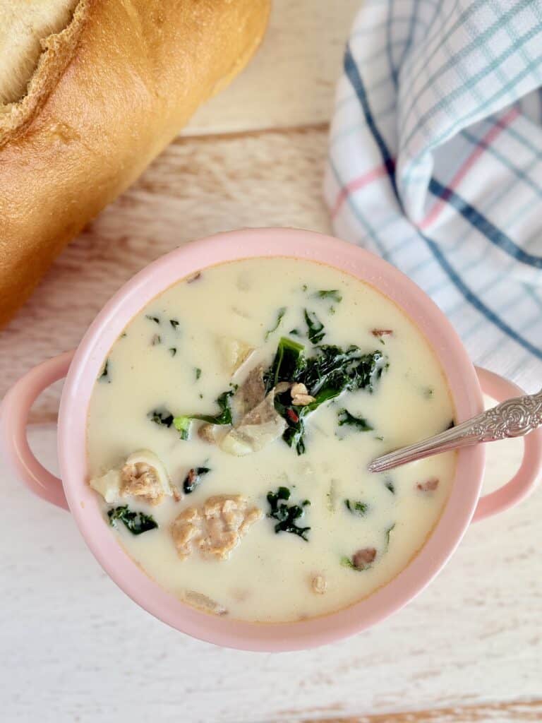 Creamy chicken and vegetable soup served in a pink bowl with a silver spoon, decorated with spinach, chicken, and herbs, perfect for comforting homemade lunches or dinners.