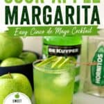 Sour Apple Margarita cocktail with lime slices and green apple garnish, served in a glass with a salted rim, on a bar counter with green apples and cocktail ingredients.