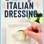 Creamy Italian dressing with a cucumber slice being dipped, served in a small white bowl, with fresh cucumbers in the background.