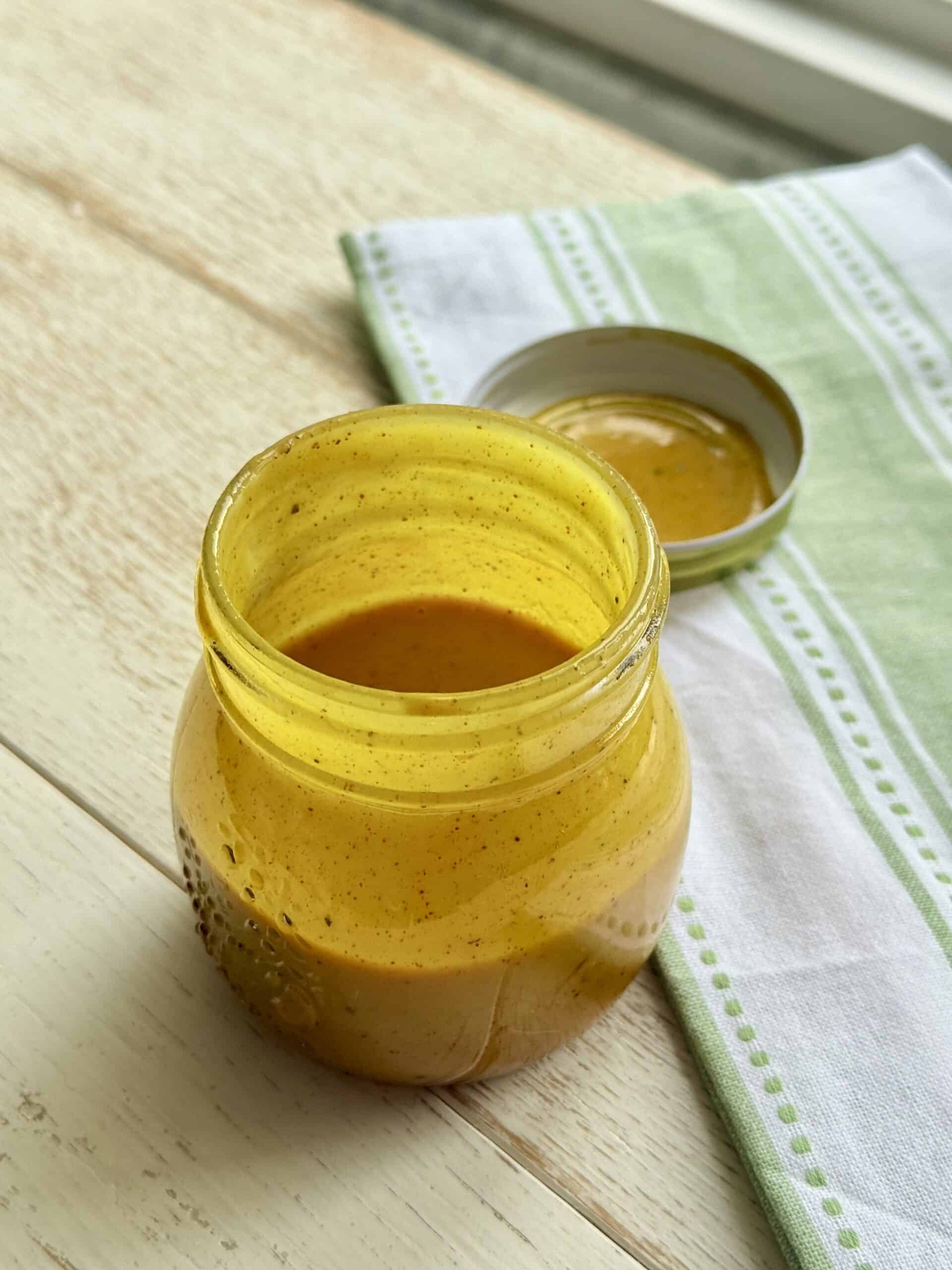 Homemade Honey Mustard BBQ Sauce on the white counter in a small mason jar. With a green and white hand towel.