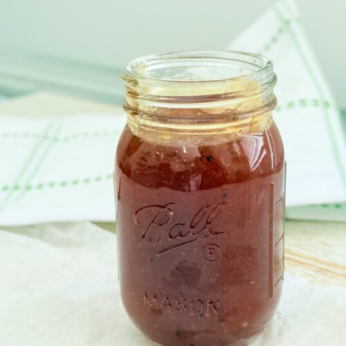 Apricot bbq sauce in a mason jar with a green and white hand towel on the counter.