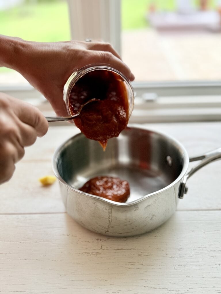Pouring blended mango bbq sauce ingredients into a sauce pan on the counter.