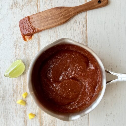 Mango BBQ Sauce in a saucepan with a wooden spoon on the counter.