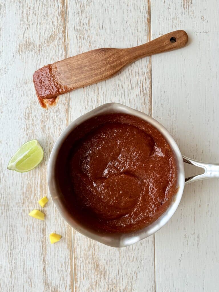 Mango BBQ Sauce in a saucepan with a wooden spoon on the counter.
