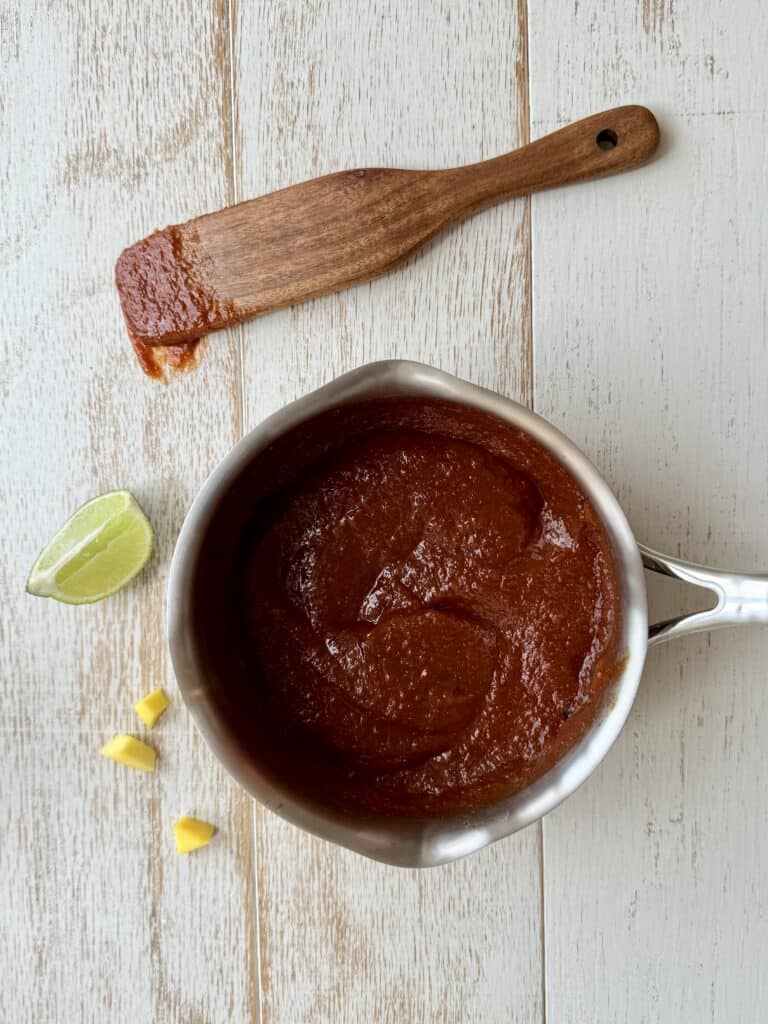 Mango BBQ Sauce in a sauce pan with a wooden spoon beside it on the counter.