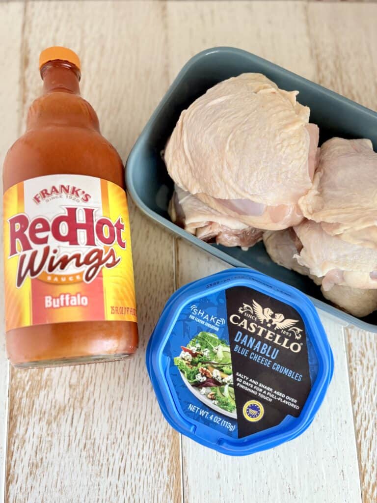 raw chicken thighs next to a bottle of buffalo sauce and a container of blue cheese
