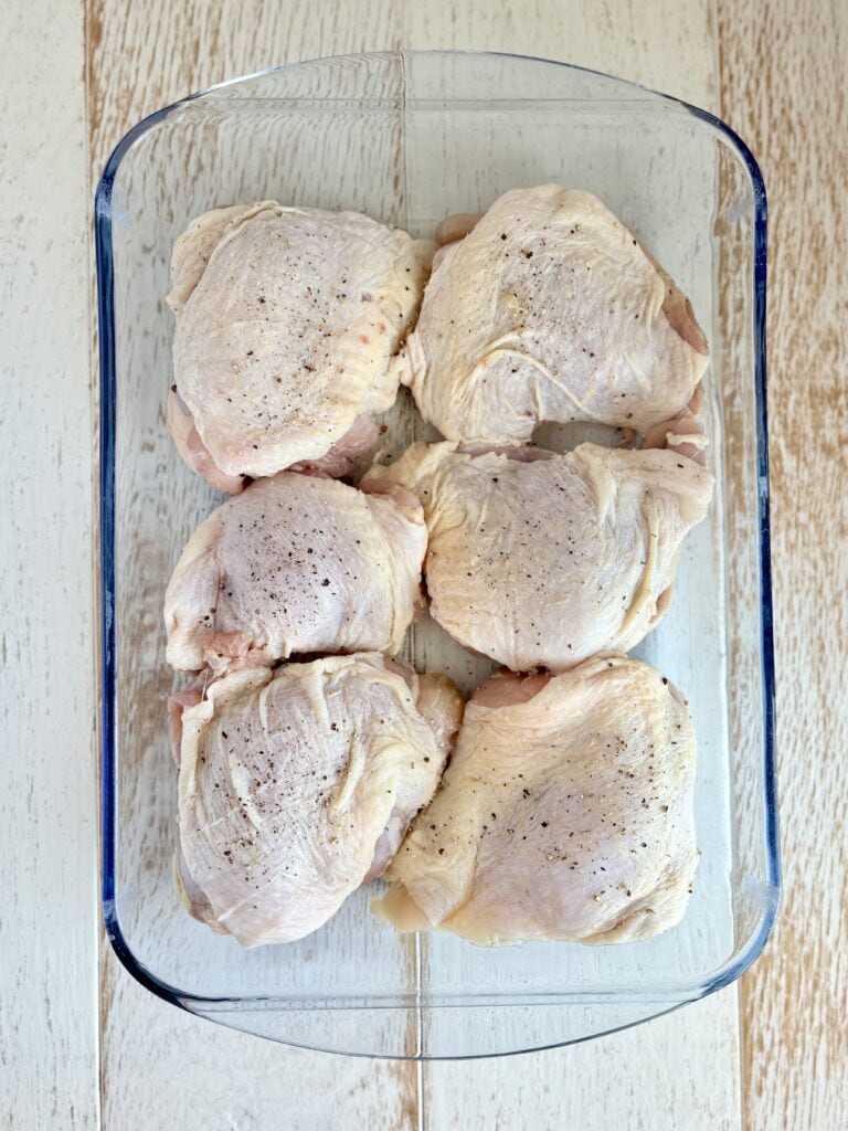 raw chicken thighs sprinkled with salt and pepper in a baking dish on a wooden board