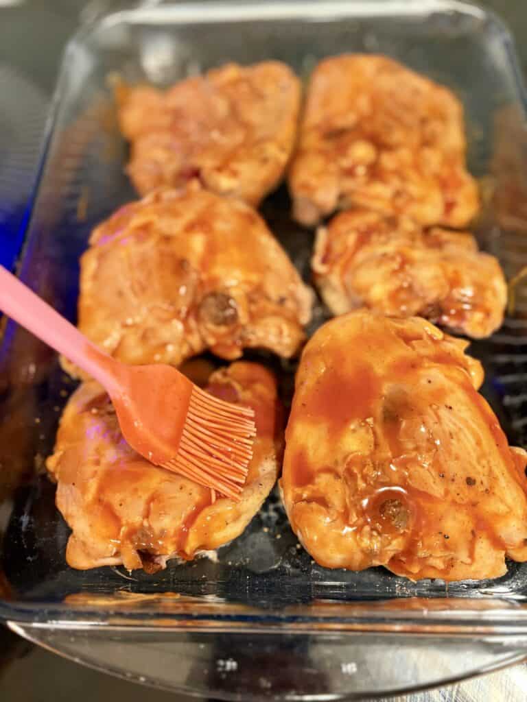 chicken thighs in a glass dish being brushed with buffalo sauce