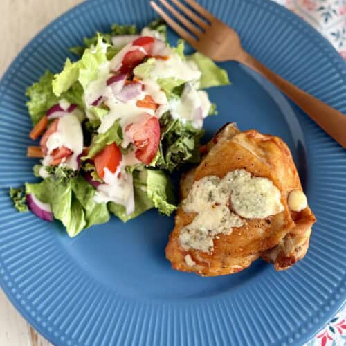 Baked Buffalo chicken thighs next to a salad with blue cheese dressing.