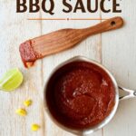 Mango BBQ Sauce in a white bowl with a wooden spatula, lime wedge, and small yellow peppers on a rustic wooden background. Perfect for grilling, dipping, and adding a sweet, tangy flavor to dishes.