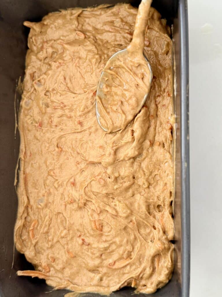 a spoon smoothing our cake batter in a loaf pan on the counter.