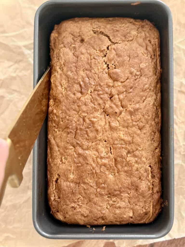 a knife loosening the edges of the loaf on parchment paper on the counter.