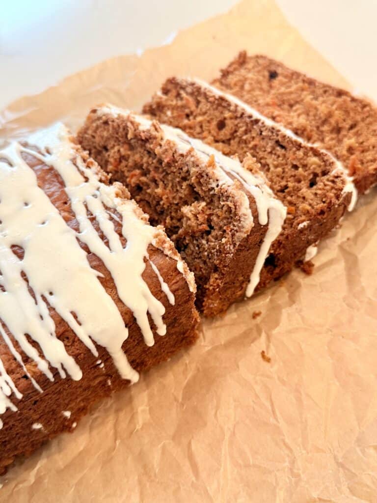 Easy carrot cake loaf with cream cheese drizzle on parchment paper on the counter.