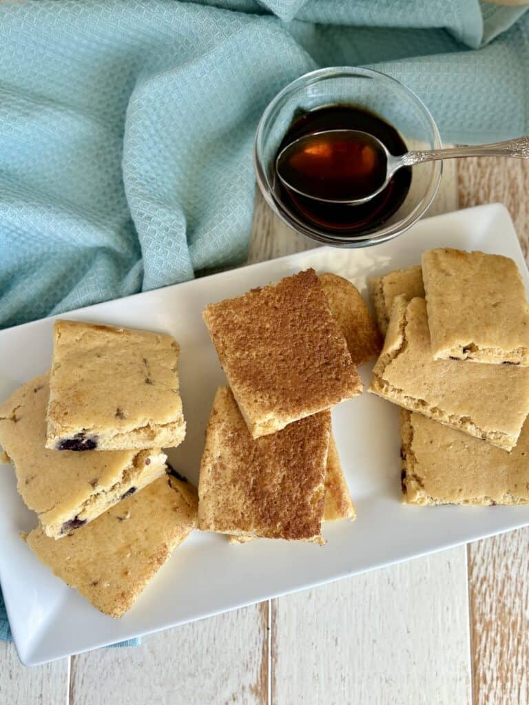 sheet pan pancakes sliced into squares on a plate next to a bowl of syrup