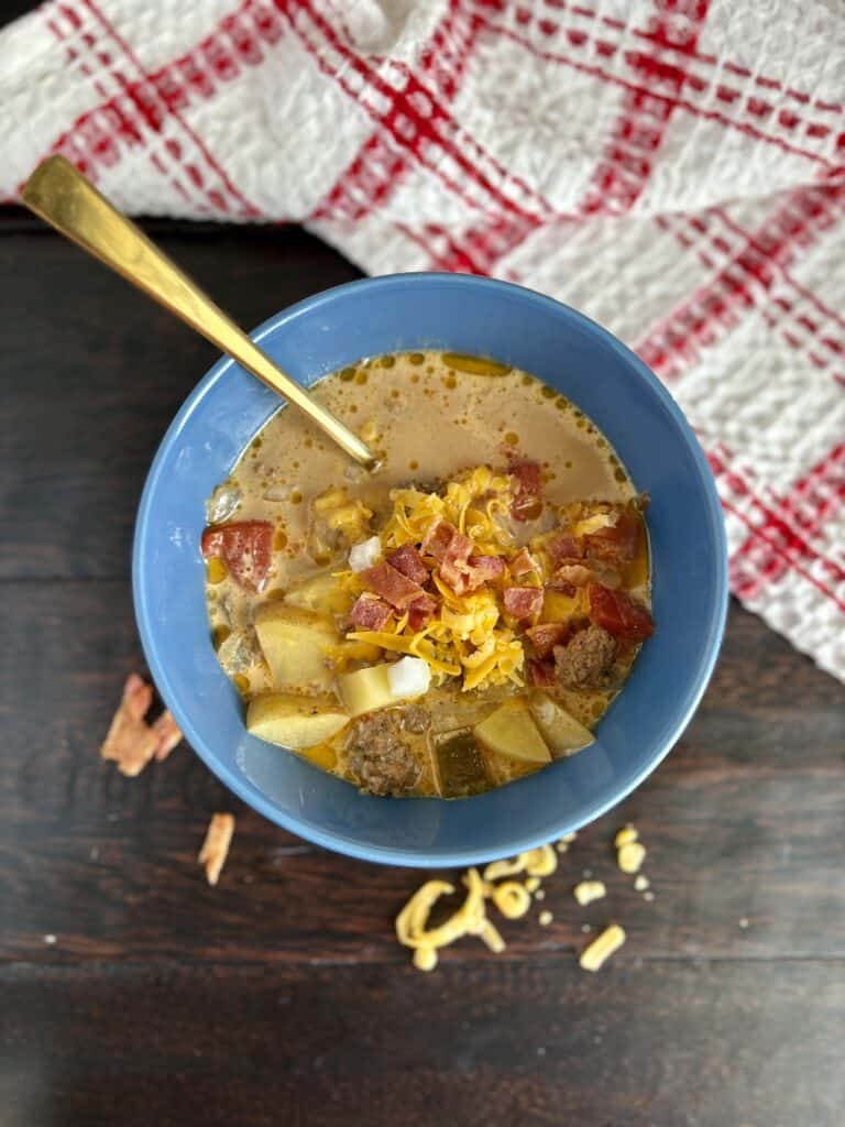 Savory chili with beef and cheese in a blue bowl, served with a spoon on a dark wooden table.