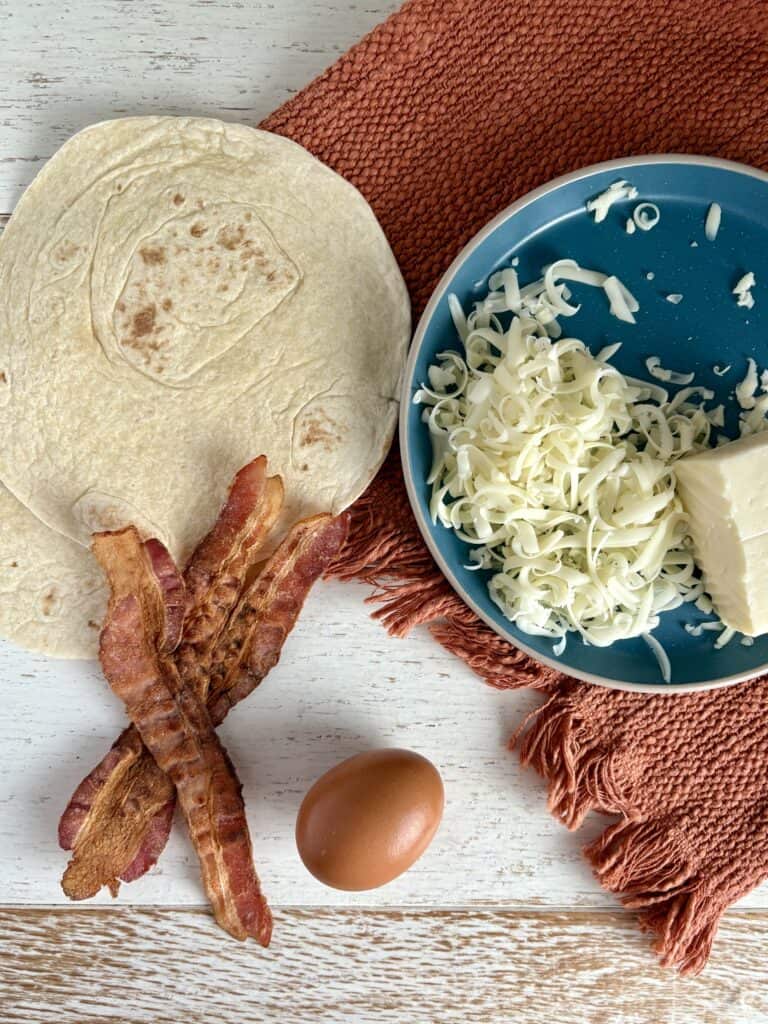 flour tortillas, cooked bacon, an egg, and shredded cheese on a blue plate