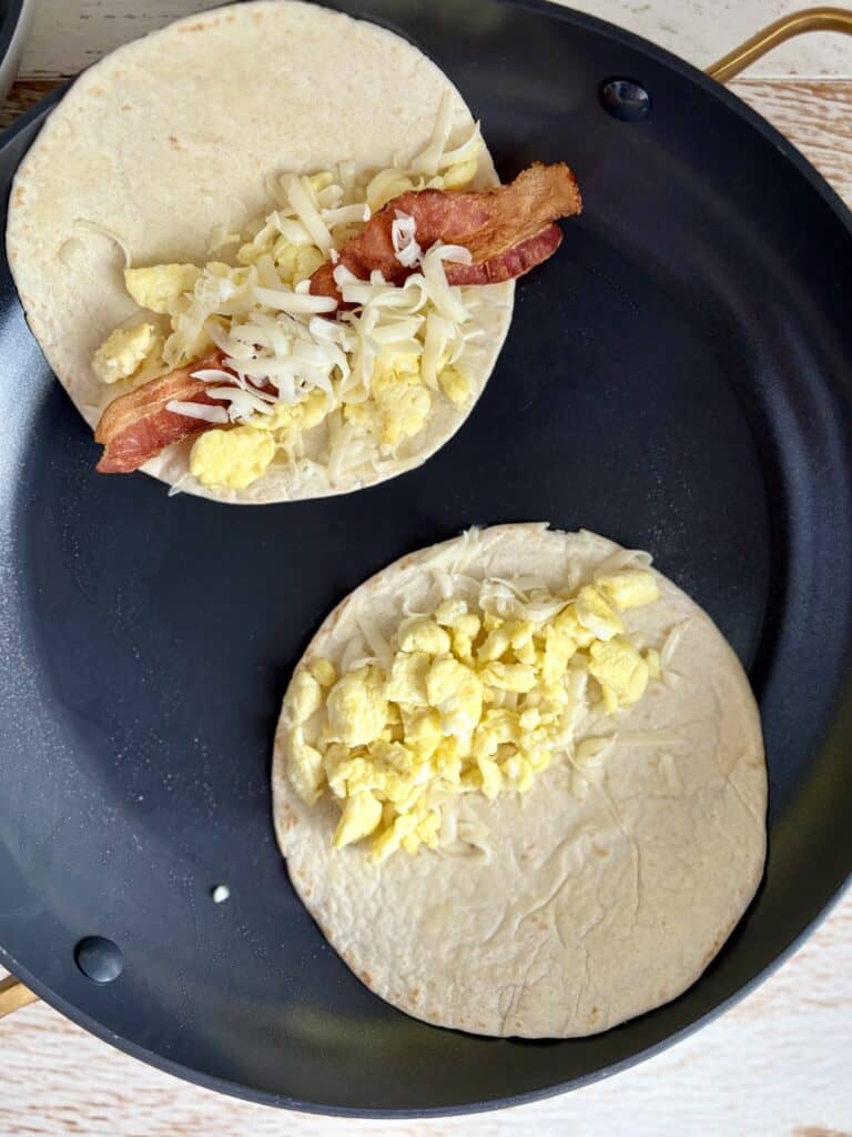 2 flour tortillas in a skillet with bacon egg and cheese