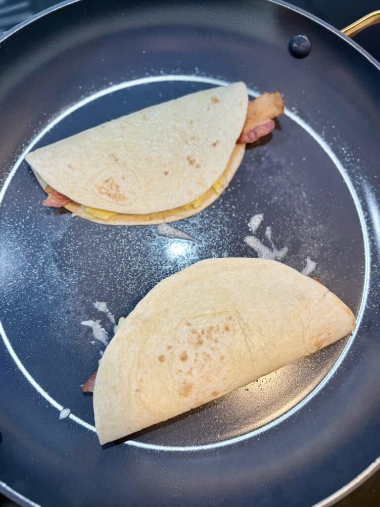2 quesadillas in a skillet browning on one side.