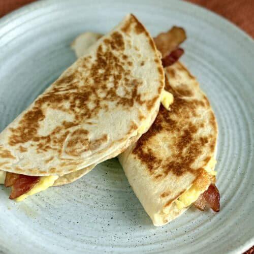 Fluffy breakfast quesadillas with eggs, bacon, and cheese on a rustic ceramic plate.
