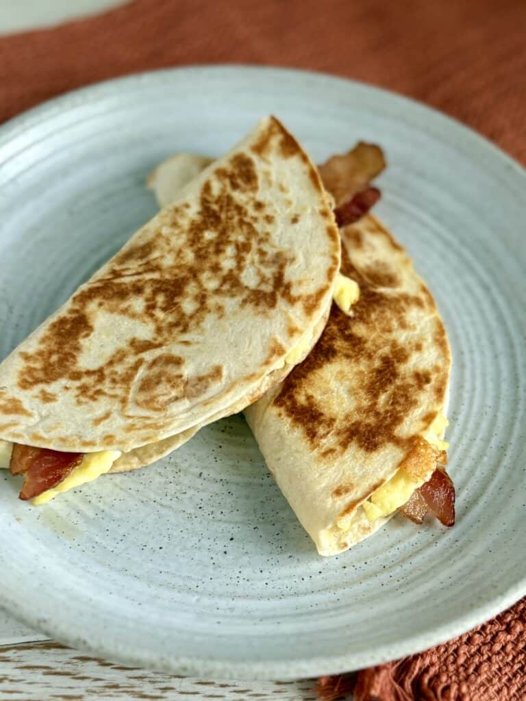 Fluffy breakfast quesadillas with eggs, bacon, and cheese on a rustic ceramic plate.
