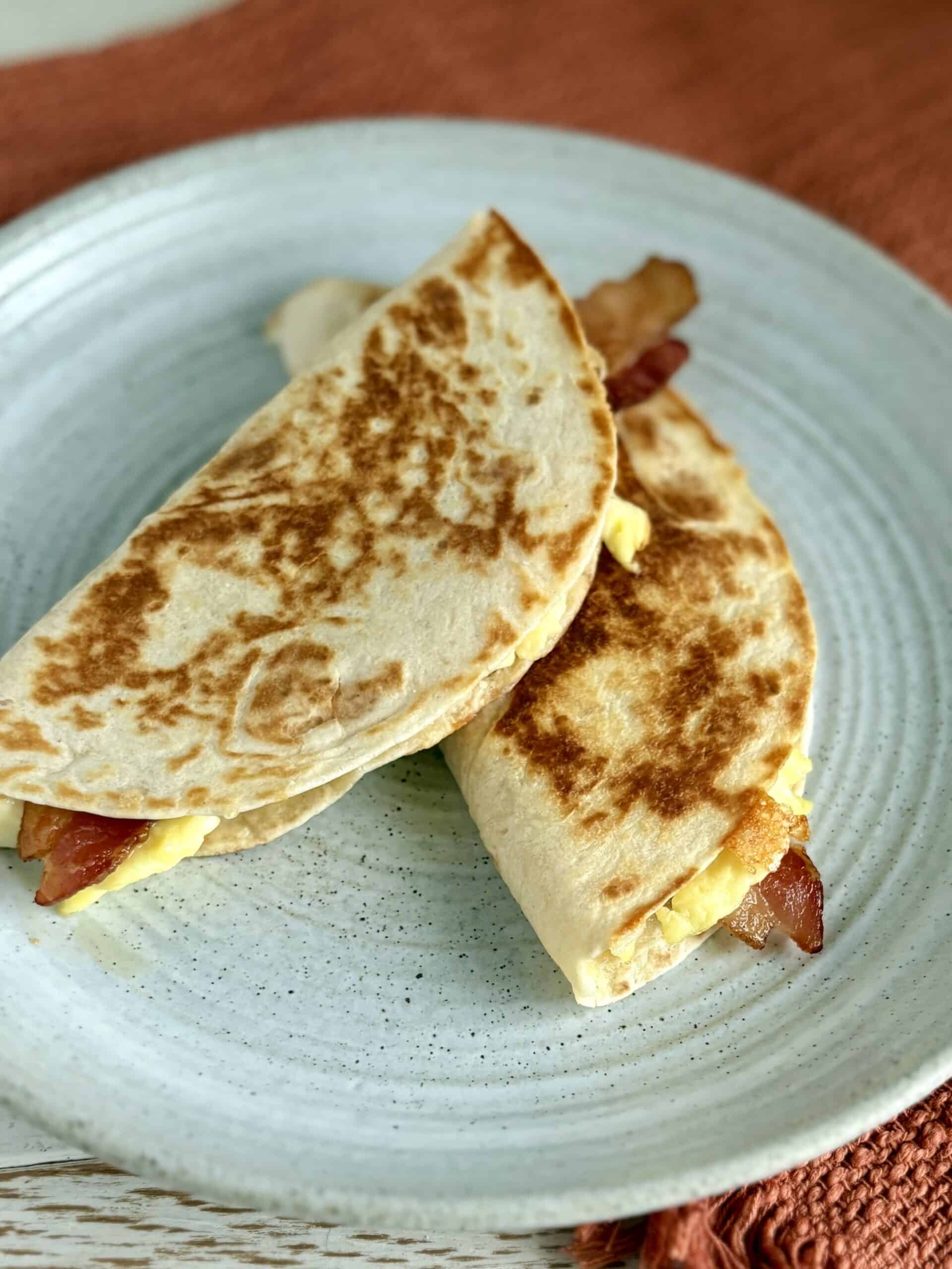 Fluffy breakfast quesadillas with eggs, bacon, and cheese on a rustic ceramic plate.