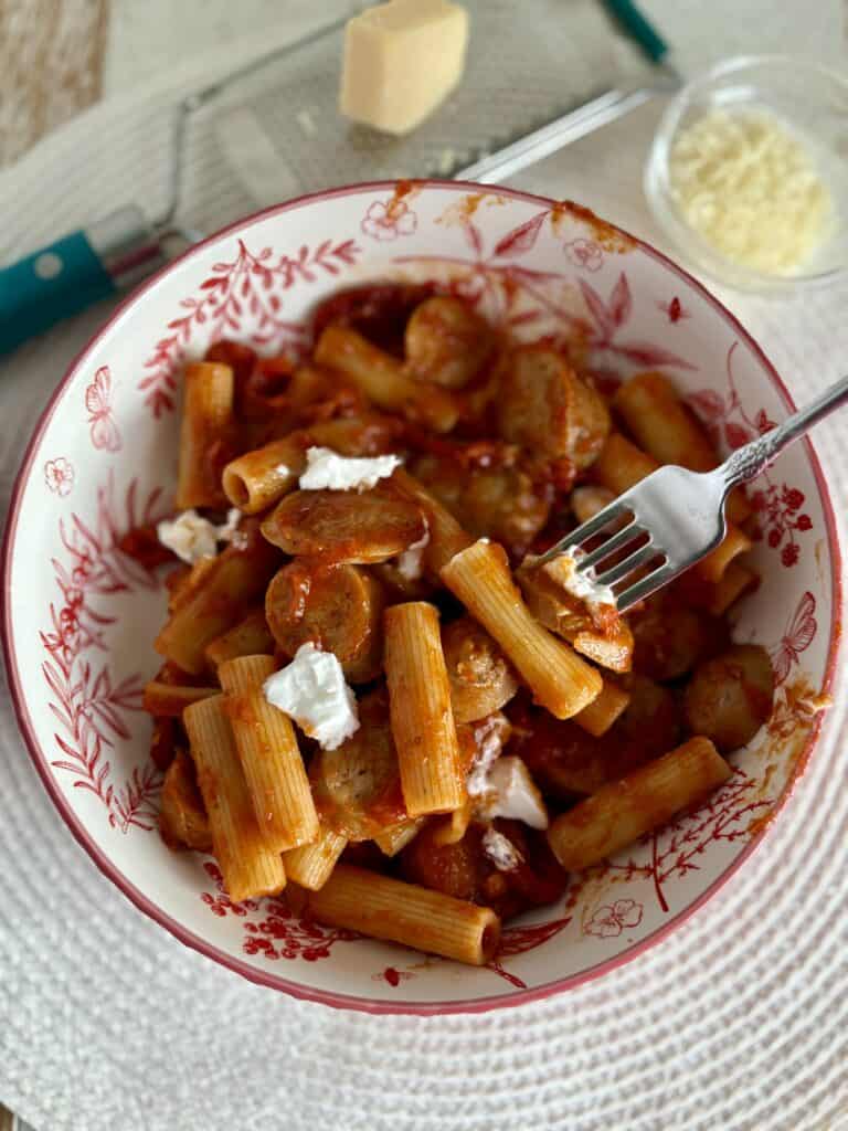 rigatoni covered in red sauce with sliced sausage and goat cheese in a meal bowl