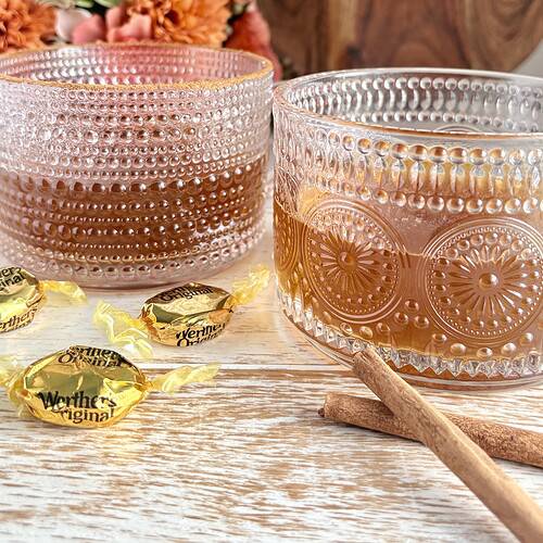 2 glass mugs containing spiked caramel cider with cinnamon sticks and caramel candies