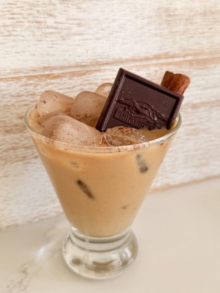 Rich, creamy Maple rum coffee cocktail with ice cubes, topped with a cinnamon stick and a piece of Ghirardelli chocolate for a delicious coffeehouse-inspired treat.